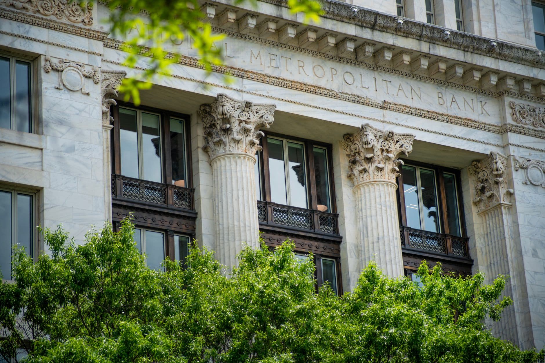 Fluted marble columns and inscribed frieze of the National Metropolitan Bank facade seen above street trees.