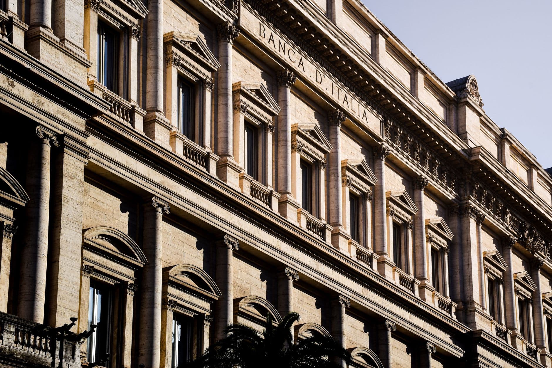 Raking afternoon light across the classical travertine facade of the Banca d'Italia headquarters in Rome.
