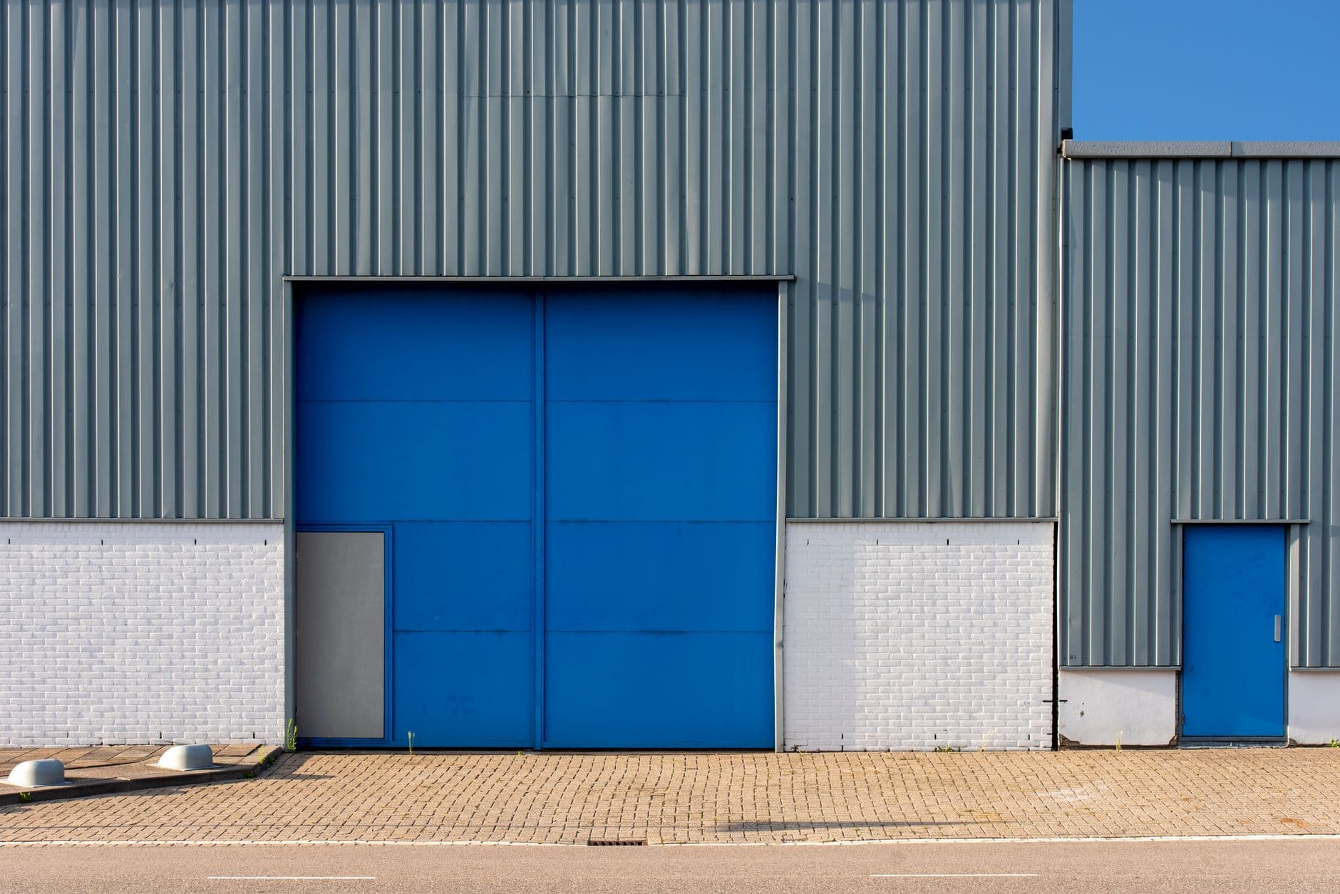 Frontal view of a gray corrugated-metal warehouse with a large blue sliding freight door and a white brick base.