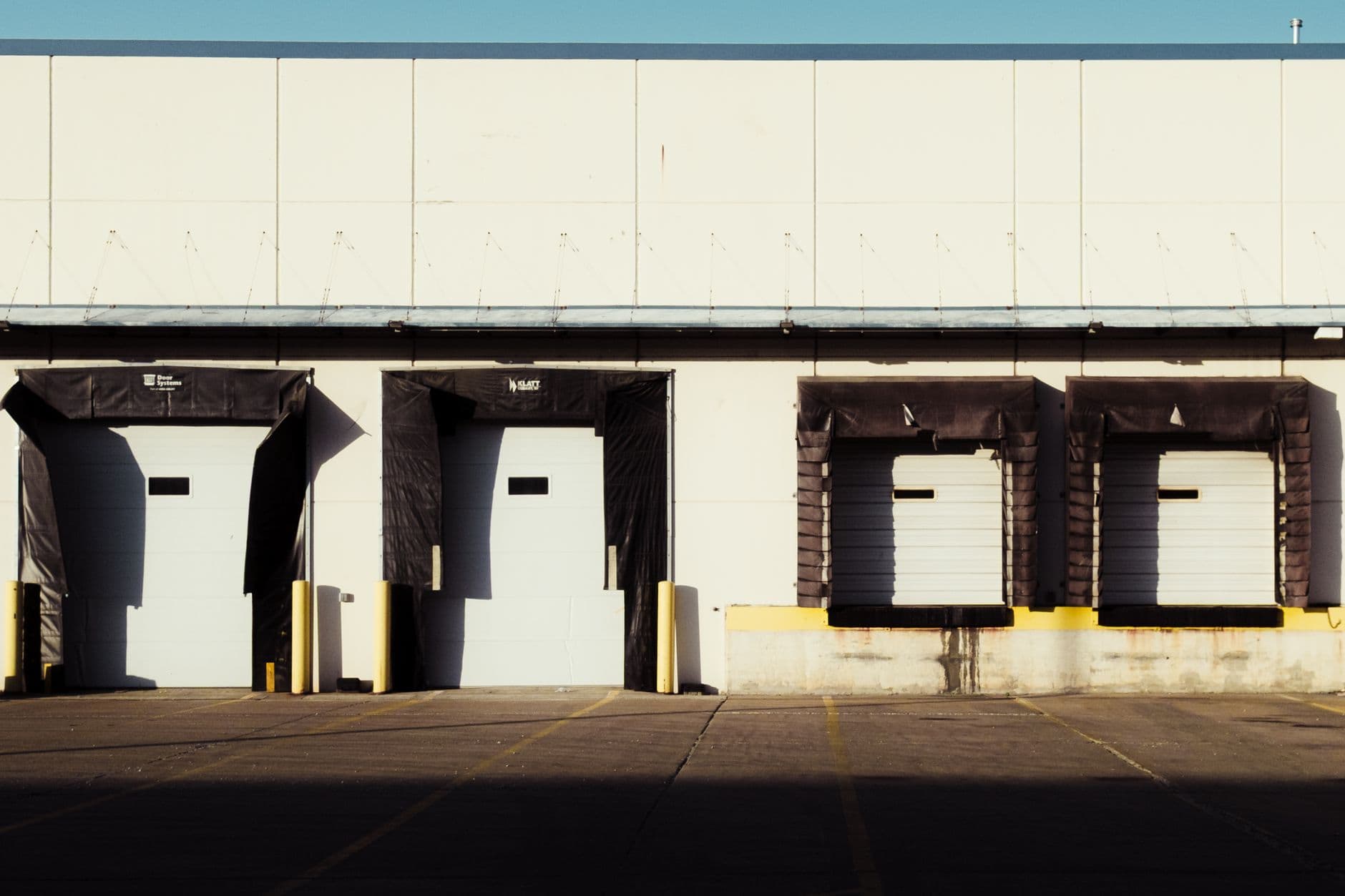 Frontal view of four sealed loading-dock bays on the sunlit facade of a distribution warehouse.