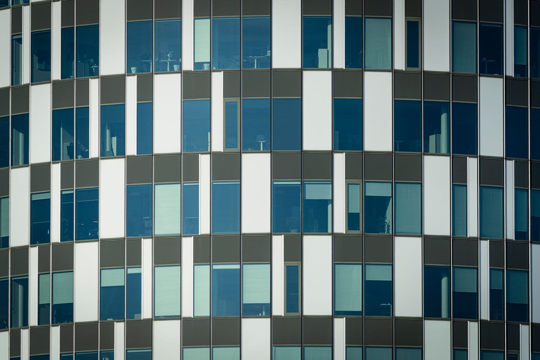 Curved office facade with an offset grid of blue-tinted glass panels and gray spandrels.